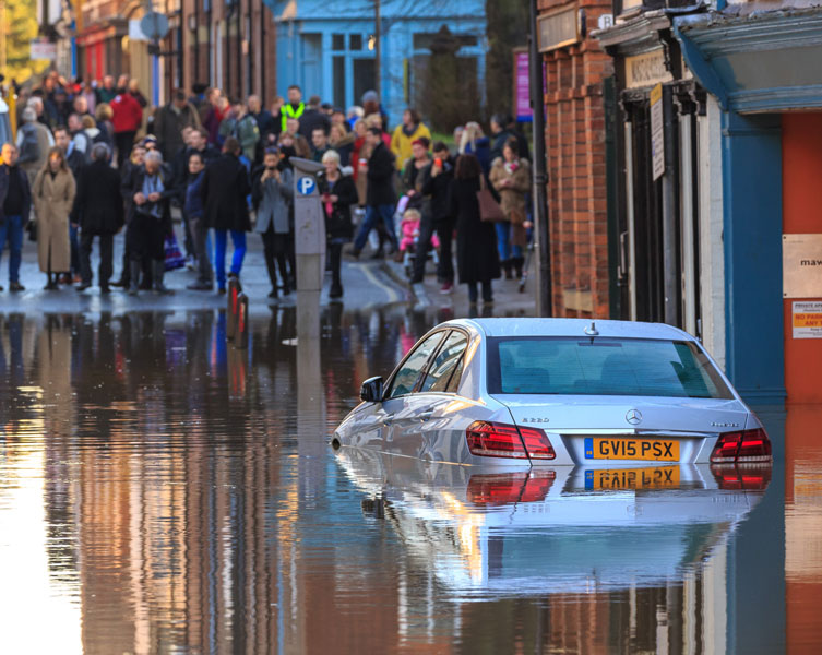 A flooded road leaves a car stranded as people gather and watch